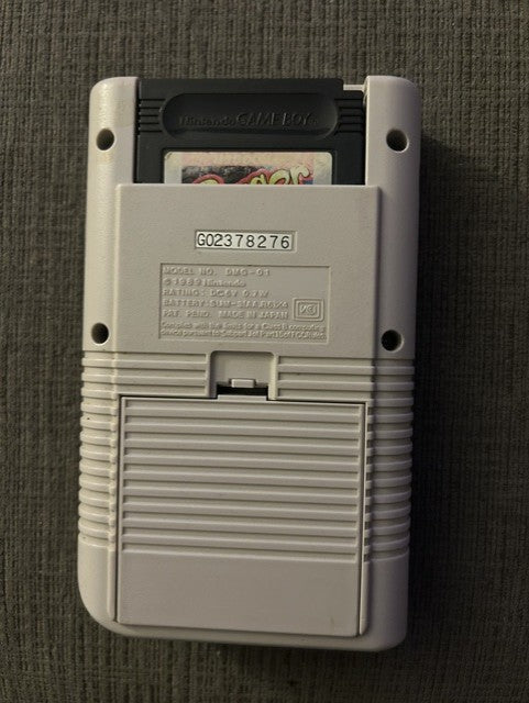 Rear of classic gray Nintendo Game Boy Unit E with identification label and battery cover